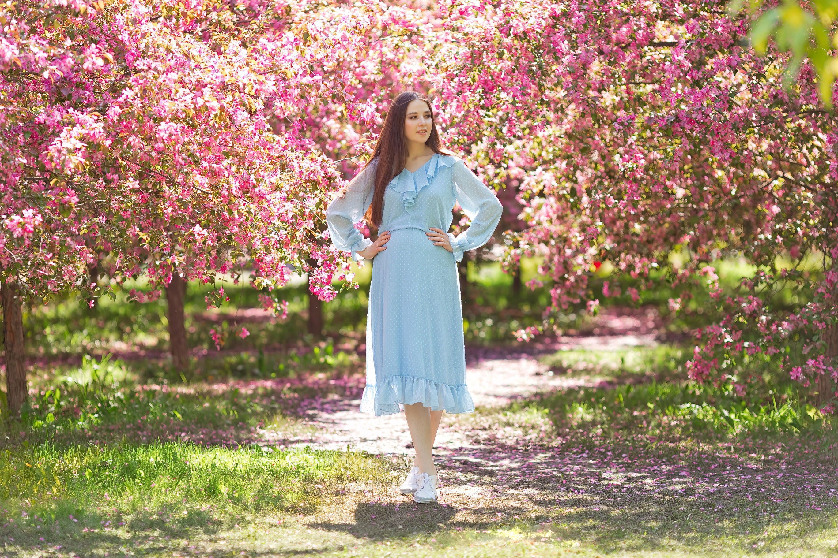 J&M fashion Spring collection dress in a light blue .A model standing in a garden with pink flowering trees.